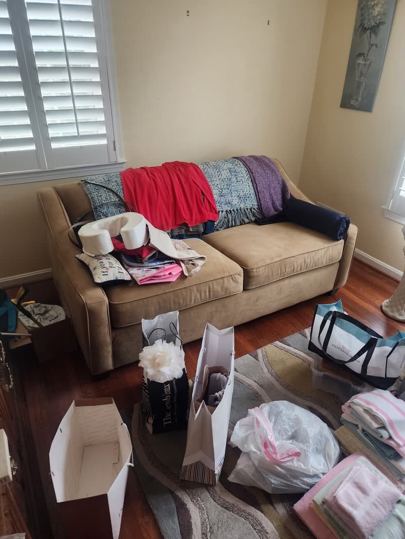 Living room mid estate cleanout with clothing, bags and boxes sorted across a sofa and floor