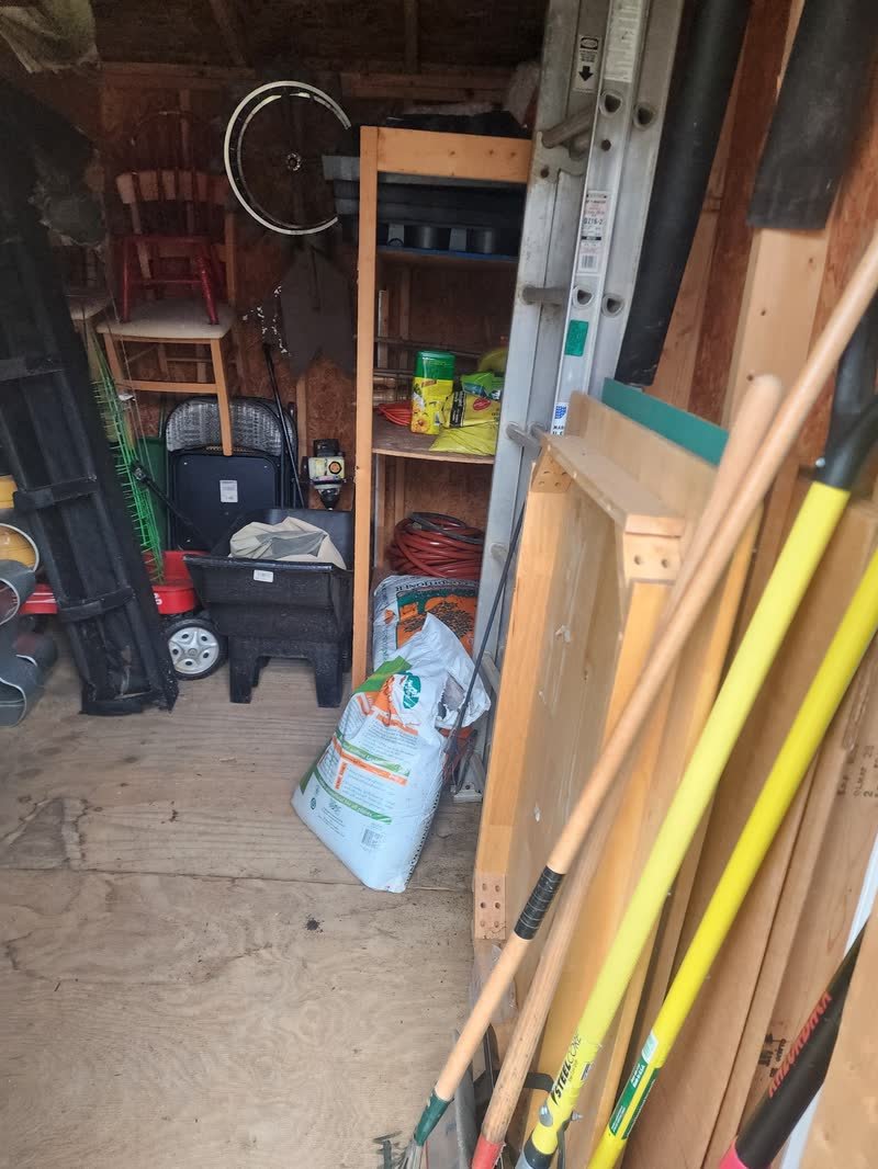 Garden tools, shelving, paint tins and stored equipment inside a garage before a clear-out